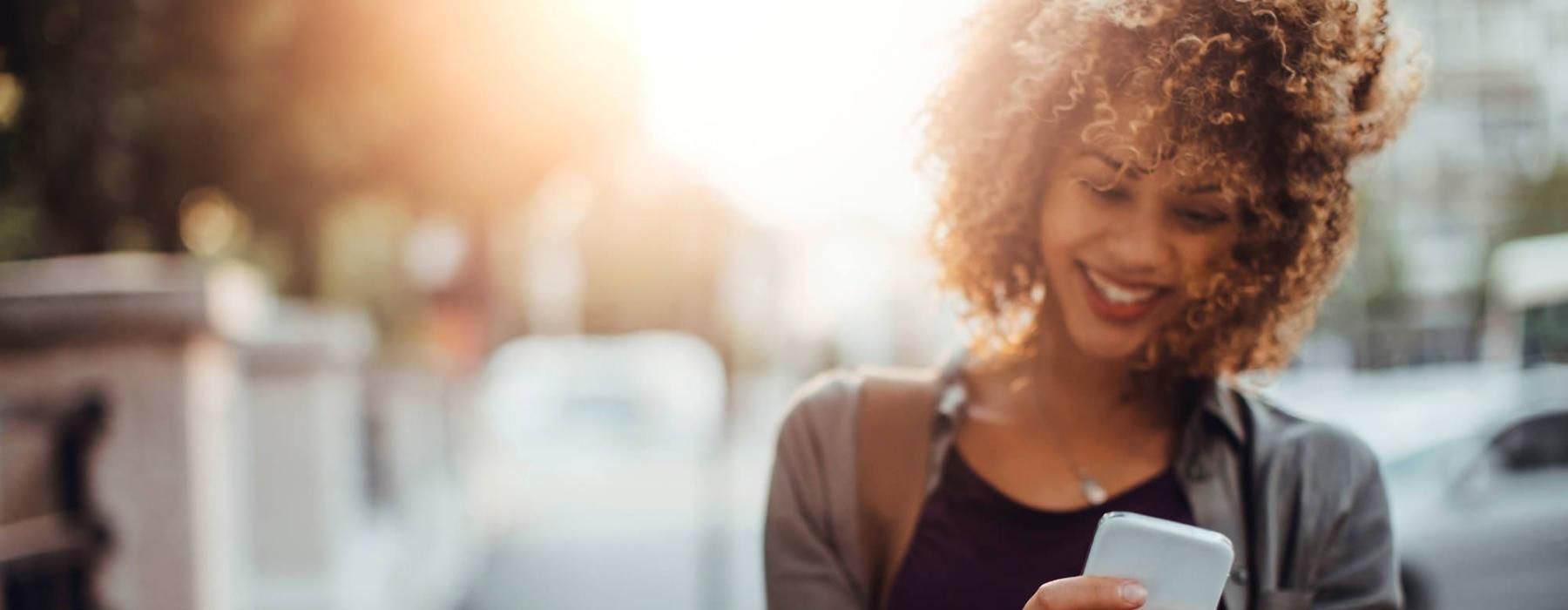 woman texts on her phone as she walks through the city